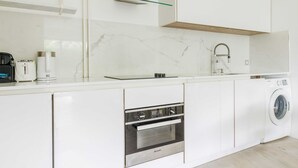A modern kitchen with white cabinetry, a built-in oven, a washing machine, and a glass shelf. - A Haven of Peace in Neuilly sur Seine (Neuilly-sur-Seine)