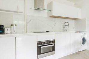 A modern kitchen with white cabinetry, a built-in oven, a washing machine, and a glass shelf. - A Haven of Peace in Neuilly sur Seine (Neuilly-sur-Seine)