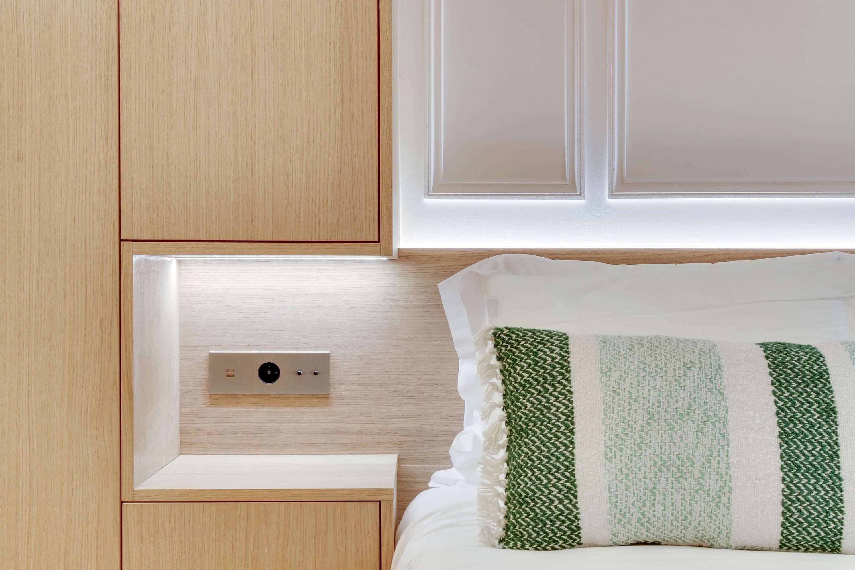 Un dormitorio con mesita de noche de madera, una mesilla auxiliar y una cama con almohada verde y blanca a rayas.