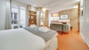 A hotel room with a large bed, a bathroom with a vanity, and a view of the street. - Historical Apartment in the Heart of Paris - 3 (Paris)