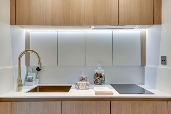 A modern kitchen with wooden cabinets, a stainless steel sink, and a black countertop. - Historical Apartment in the Heart of Paris - 3 (Paris)