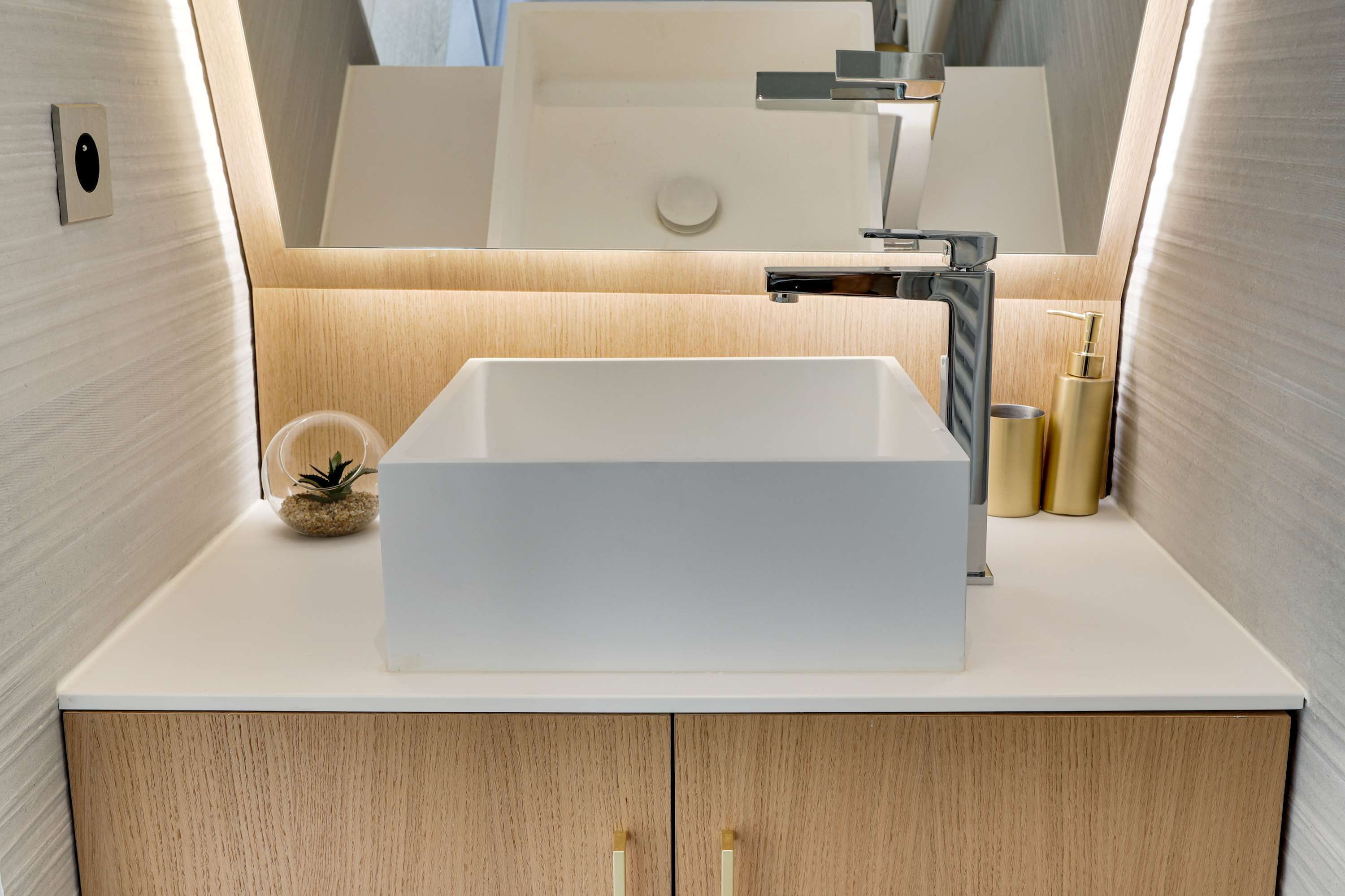 A modern bathroom with a white sink, wooden vanity, and a mirror above the sink.