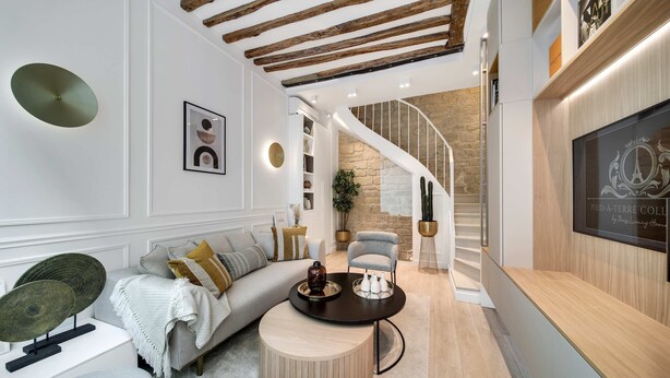 A modern living room with a sofa, coffee table, and a staircase leading to an upper floor. - Historical House in the Heart of Paris - 5 (Paris)