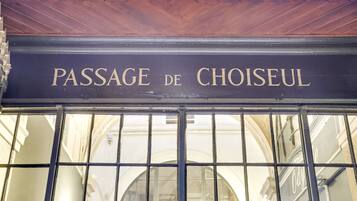 Un cartel con la inscripción 'PASSAGE DE CHOISEUL' sobre un ventanal con celosía metálica.