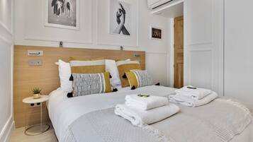 Une chambre d’hôtel bien rangée, avec un grand lit, une table de chevet agrémentée d’une plante et deux tableaux encadrés au mur.