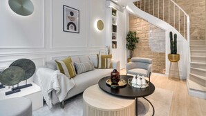 A modern living room with a white sofa, a round coffee table, and a staircase with a stone wall. - Historical House in the Heart of Paris - 5 (Paris)