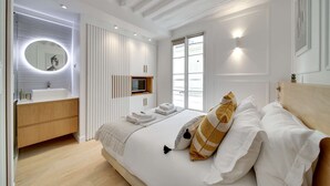 A modern bedroom with a large bed, a built-in vanity, a round mirror, and a television. - Historical House in the Heart of Paris - 5 (Paris)