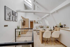 Une cuisine moderne avec un coin repas, comprenant une table en bois, des chaises blanches et une grande fenêtre.