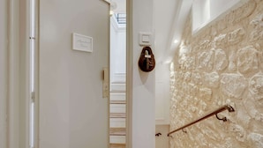 A hallway with a stone wall, a door with a sign, and a shoe rack. - Historical Apartment in the Heart of Paris - 4 (Paris)