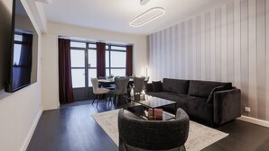 Ett modernt vardagsrum med en soffa i mörk färg, ett soffbord i glas och en matplats med bord och stolar.
