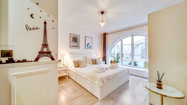 Un dormitorio con una cama grande, una mesita de vidrio, vistas a la ciudad y una decoración de la Torre Eiffel.