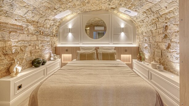 A bedroom with a stone wall, a large bed, two bedside tables, and a mirror above the bed. - Historical Apartment in the Heart of Paris (Paris)