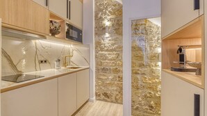 A modern kitchen with marble countertops, wooden cabinets, and a stone accent wall. - Historical Apartment in the Heart of Paris (Paris)
