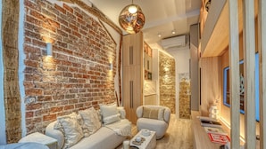 A cozy living room with a brick wall, a sofa, a coffee table, and a wooden sideboard. - Historical Apartment in the Heart of Paris (Paris)