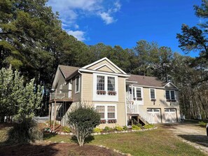 A two-story house with a front porch, a garage, and a small front yard with a tree and shrubs. - Camp Chesapeake 6 bedroom Private Waterfront - Dock, Hot Tub, Family Friendly (Onancock)
