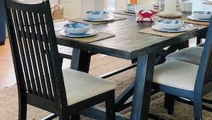 Ein Essbereich mit einem Holztisch, gedeckt für vier Personen, umgeben von schwarzen Stühlen mit hellen Kissen.