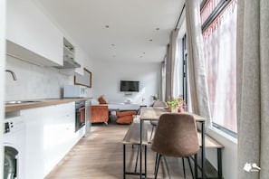 Moderni keittiö, jossa on valkoiset kaapit, puinen työtaso ja sisäänrakennettu uuni. Keittiössä on ruokailutila, jossa on pöytä ja tuolit, sekä suuri ikkuna, jossa on verhot.