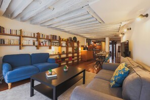 Una sala de estar con un sofá azul, un sofá gris, una mesa de centro y una estantería llena de libros y objetos decorativos.