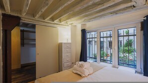 Une chambre avec un grand lit, une commode et une vue sur une cour intérieure, visible par une fenêtre.