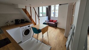 Een kleine keuken met een wasmachine, een eettafel met stoelen, een bank en een trap.