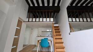 Een modern interieur met een trap naar een hoger gelegen verdieping, een eethoek met een blauwe stoel, en een keuken met witte kasten.