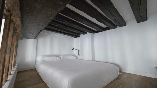 Een slaapkamer met een groot bed, houten balken in het plafond en een witte muur.