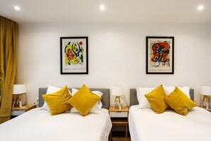 A hotel room with two beds, each with white bedding and yellow pillows. There are two framed artworks on the wall above the beds. - Notre Dame Neighborhood AC Apartment 10 PAX (Paris)
