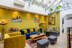 A modern living room with a blue sofa, yellow armchair, and a coffee table. There are paintings on the walls and a large mirror. - Notre Dame Neighborhood AC Apartment 10 PAX (Paris)