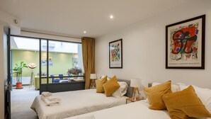 Una camera d'albergo con due letti, un'ampia finestra e opere d'arte alle pareti.