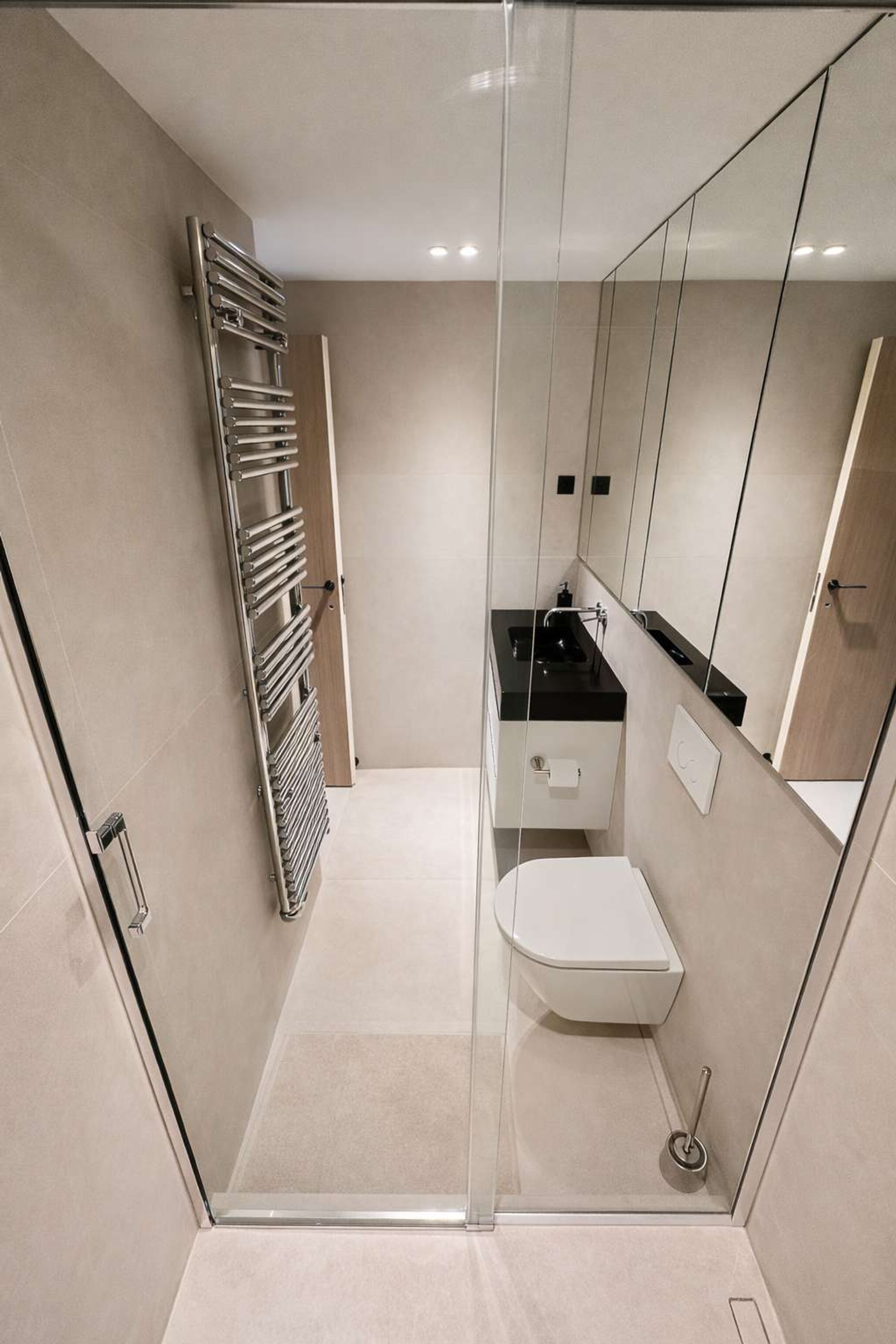 A modern bathroom with a glass shower enclosure, a white toilet, a black countertop sink, and a built-in mirror.