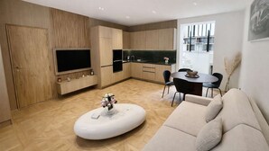 A modern living room with a sofa, a coffee table, and a TV. There is a kitchen area with a dining table and chairs. - Magnifique Loft Luxe Montmartre Climatis (Paris)