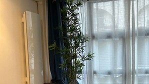 A dining area with a table, chairs, a potted plant, and a view through sheer curtains. - Flat Near Notre Dame 4 pax AC (Paris)
