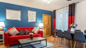 A room with a red sofa, a coffee table, a dining table with chairs, and artwork on the walls. - Place des Vosges Havre de Paix Paris 8 Pers AC (Paris)