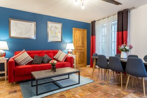 Ein Zimmer mit einem roten Sofa, einem Couchtisch, einem Esstisch mit Stühlen und Kunstwerken an den Wänden.