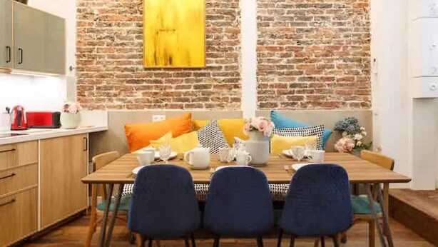 A dining area with a brick wall, a wooden table, and blue chairs. - 1st District Louvre Notre Dame 8 Guests - AC (Paris)