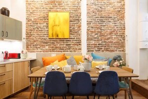 A dining area with a brick wall, a wooden table, and blue chairs. - 1st District Louvre Notre Dame 8 Guests - AC (Paris)