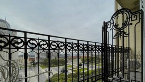Een balkon met een smeedijzeren hekwerk, een fiets en een stadsgezicht met gebouwen en een weg.