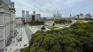 Stadsgezicht met een groot open plein, omringd door gebouwen, waaronder een opvallend klassiek gebouw aan de linkerkant en moderne wolkenkrabbers op de achtergrond.