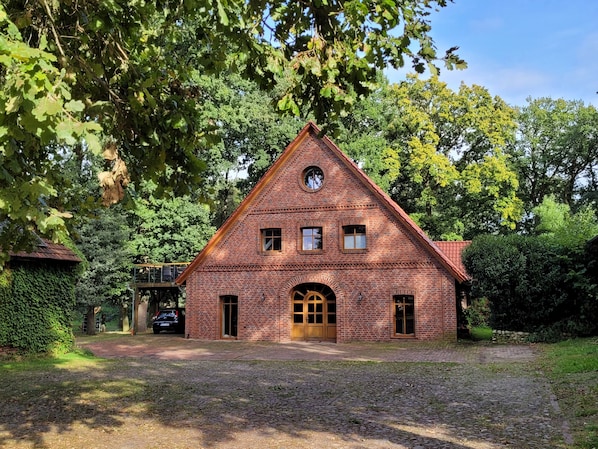 Un bâtiment en briques surmonté d’un toit triangulaire, avec une porte centrale et des fenêtres au deuxième étage.