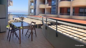 A balcony with a table and chairs, overlooking a coastal area with a building in the background.
