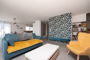 A modern living room with a sofa, a yellow armchair, a white coffee table, and a bookshelf.