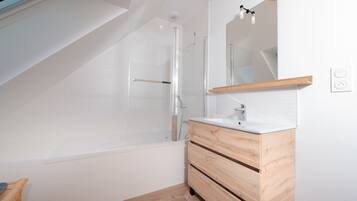 A modern bathroom with a glass shower enclosure, a wooden vanity, and a large mirror.