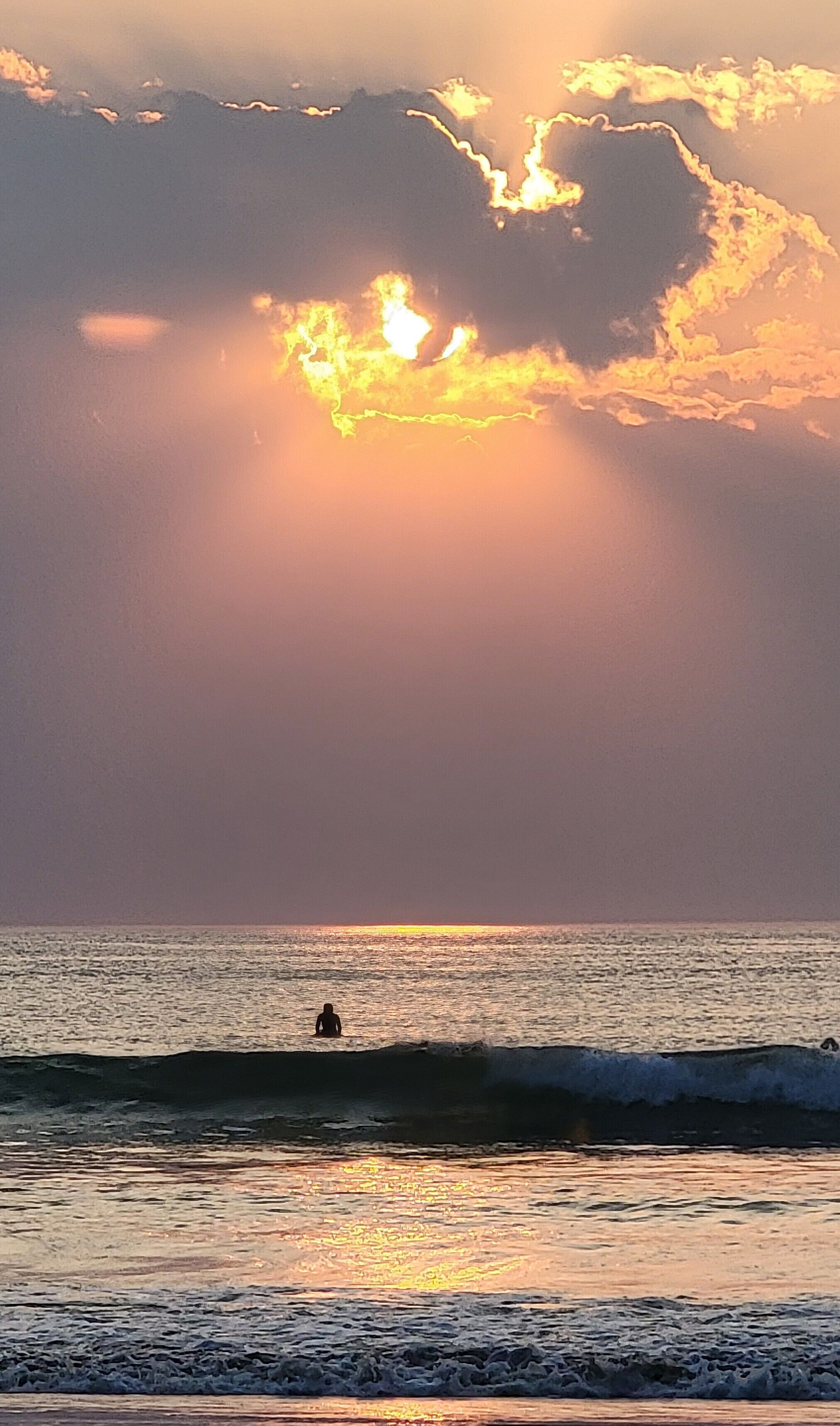 A beach scene with a person in the water, waves, and a sunset.