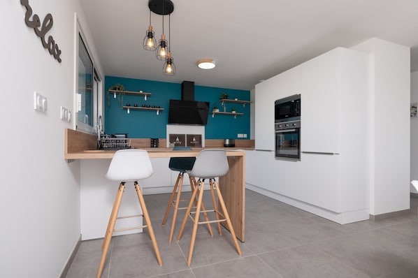 A modern kitchen with a teal accent wall, a black range hood, and a built-in oven.