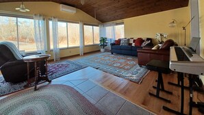 A spacious living room with a wooden ceiling, large windows, a piano, a sofa, and a coffee table.