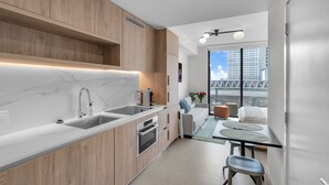 Et moderne køkken med bordplade i marmor, træskabe og en indbygget ovn. Der er et spiseområde med bord og stole, samt en balkon med udsigt over byen.