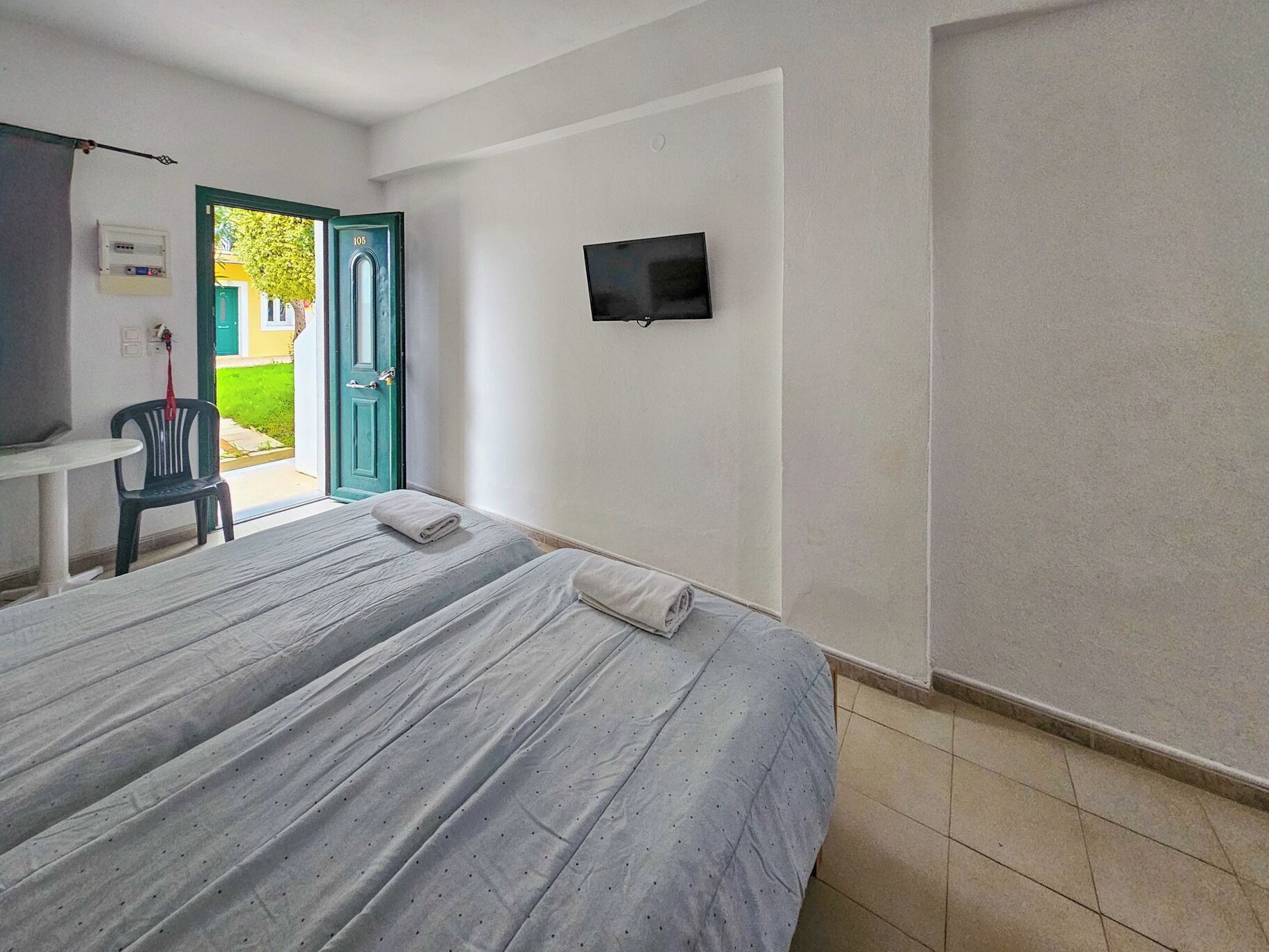 Ein Schlafzimmer mit Bett, einem an der Wand montierten Fernseher, einem Sessel und einer zur Außenseite führenden Tür.