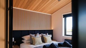 Une chambre moderne avec une tête de lit à lattes, un lit bien fait avec des oreillers et une fenêtre laissant entrer la lumière naturelle.