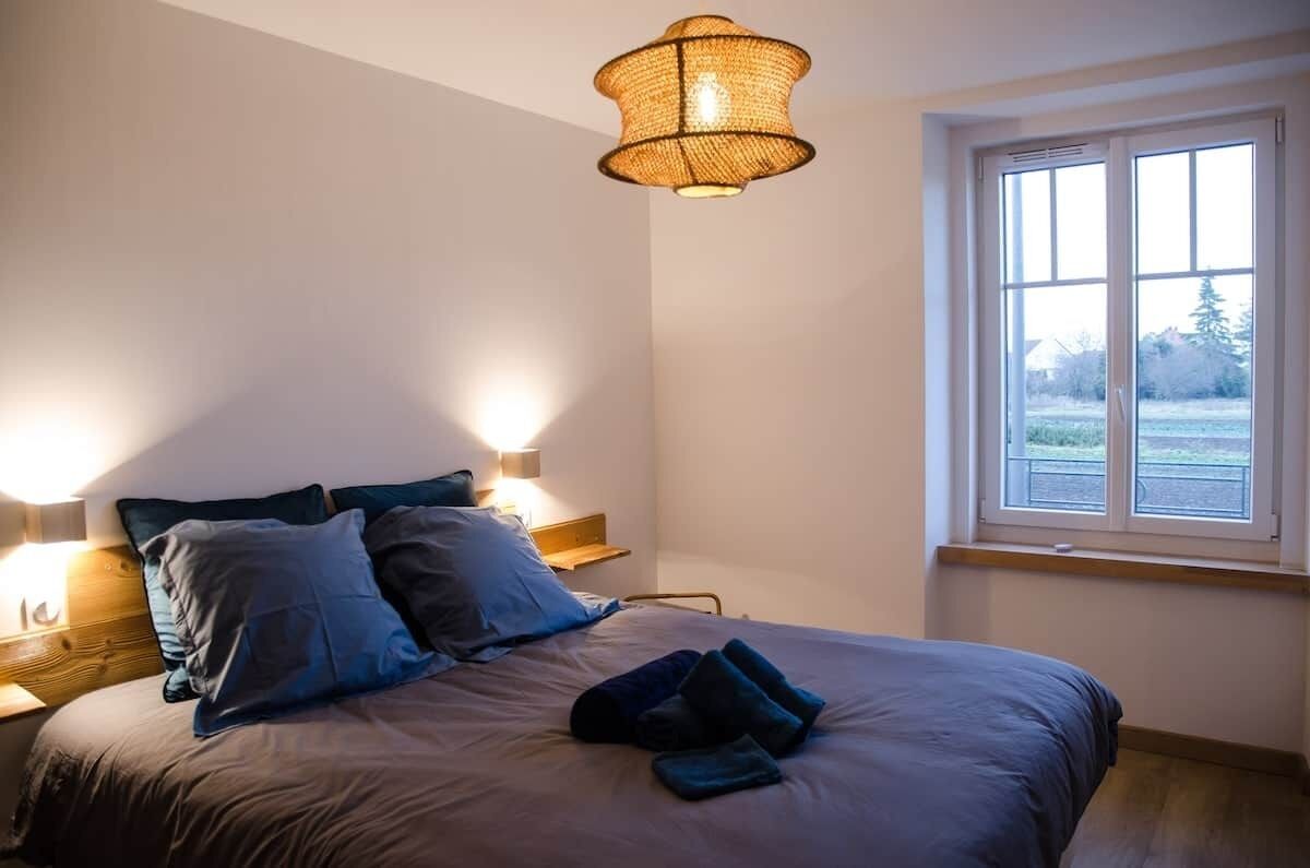 Een slaapkamer met een bed, nachtlampjes, een raam en een hangende lamp.