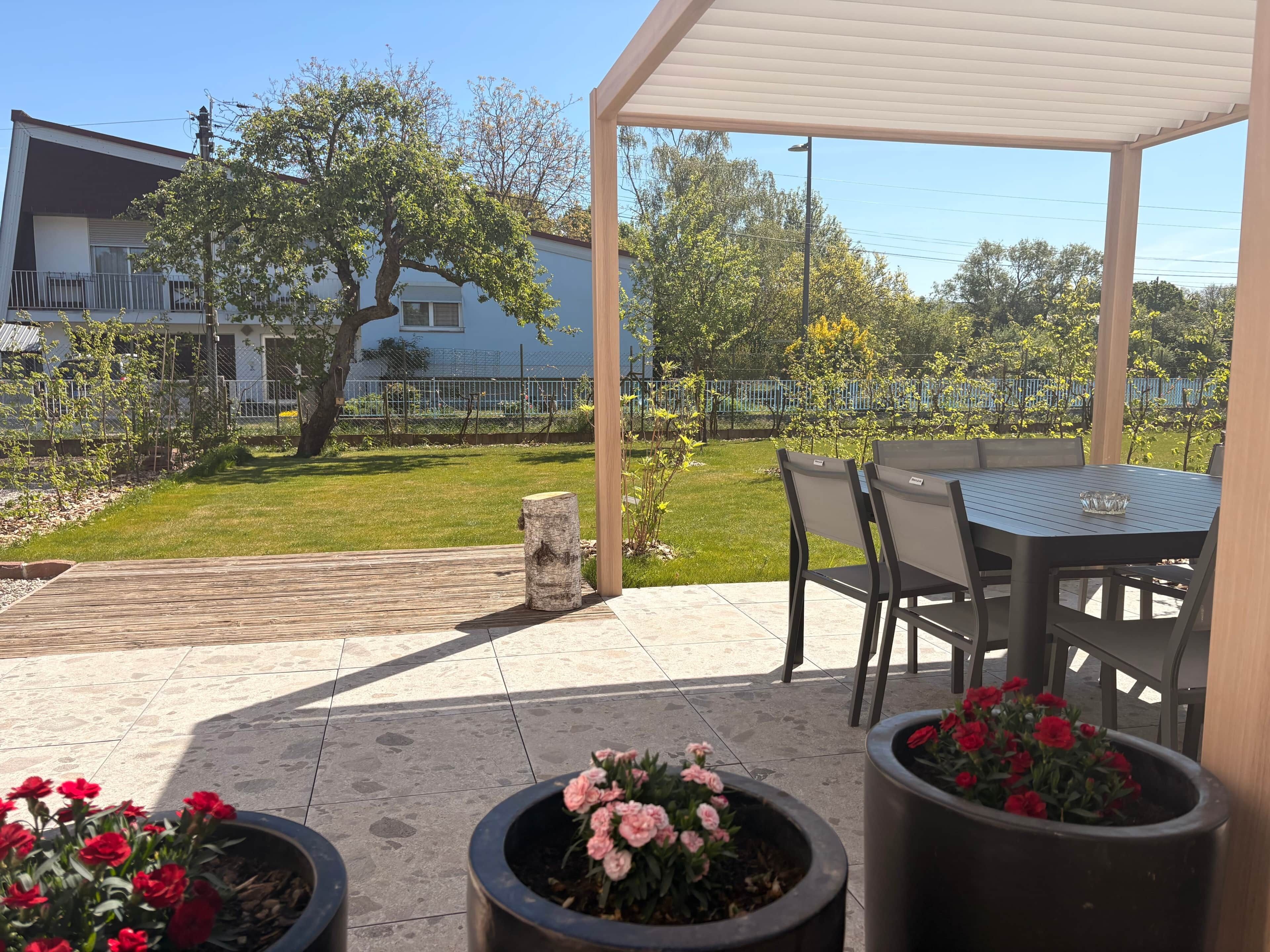 Een terras buiten met een tafel en stoelen, plantenbakken en uitzicht op een woonwijk.
